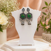 Decorative earrings on a white stand with flowers in the background