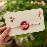 Rakhi with 'Bro' message on a card held by a hand with a blurred floral background