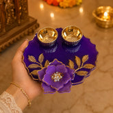 Decorative purple plate with gold floral design held by a hand, with a blurred background of lights and objects.