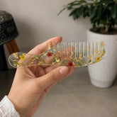 Hand holding elegant floral resin hair comb with real dried flowers, gold foil detailing, and crystal-clear glossy finish.