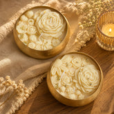 Two gold bowls with floral designs on a wooden surface with a candle and flowers.