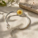 Silver bracelet with a hexagonal charm featuring a yellow flower on a beige surface.