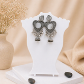 Ornate silver earrings on a white stand with a neutral background