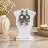 Pair of silver earrings on a white stand with a decorative background