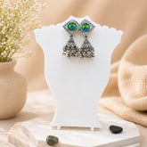 Pair of earrings with green gemstones on a white stand with a natural background