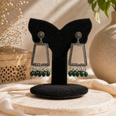 oxidised silver trapezium mirror drop earrings with green bead detailing displayed on black stand premium jewellery product image