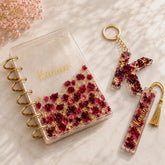 Decorative notebook with floral design, keychain, and bookmark on a marble surface.