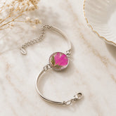 Silver bracelet with a pink floral charm on a marble surface