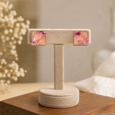 Pair of square earrings with floral design on a beige stand against a blurred indoor background