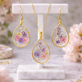 Gold-framed earrings and necklace with floral designs on a marble stand.