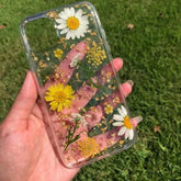 Phone case with pressed flowers held in a hand against a grass background