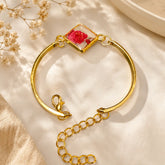 Gold bracelet with a clear heart-shaped charm featuring red flowers on a beige fabric background.