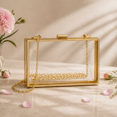 Gold clutch with clear front on a beige surface with pink flowers