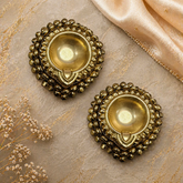 Pair of ornate gold earrings on a textured surface with flowers and fabric.