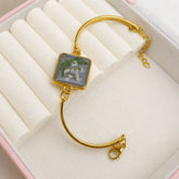 Gold bracelet with a square charm featuring floral design on a white cushioned surface.