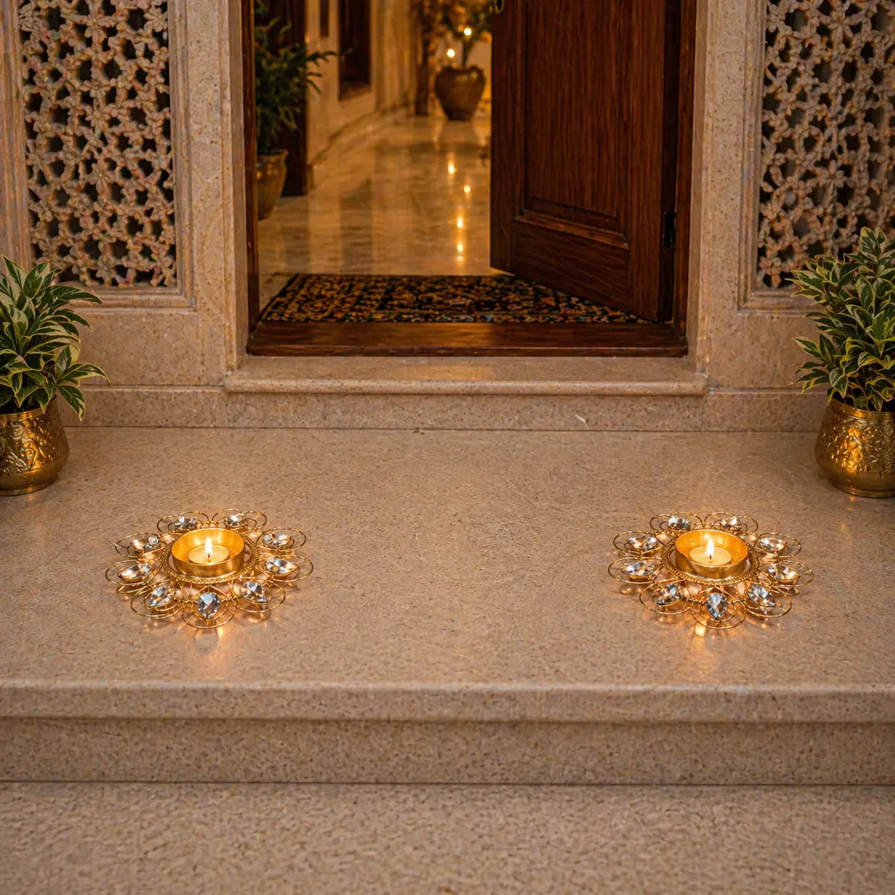Decorative candle holders with lit candles on a stone ledge, with a door and plants in the background.