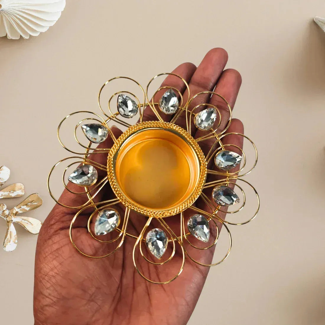 Decorative gold and crystalincense holder held in a hand against a beige background