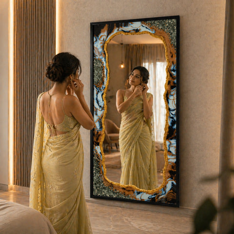 Woman in a yellow saree adjusting her earrings in front of a decorative mirror.