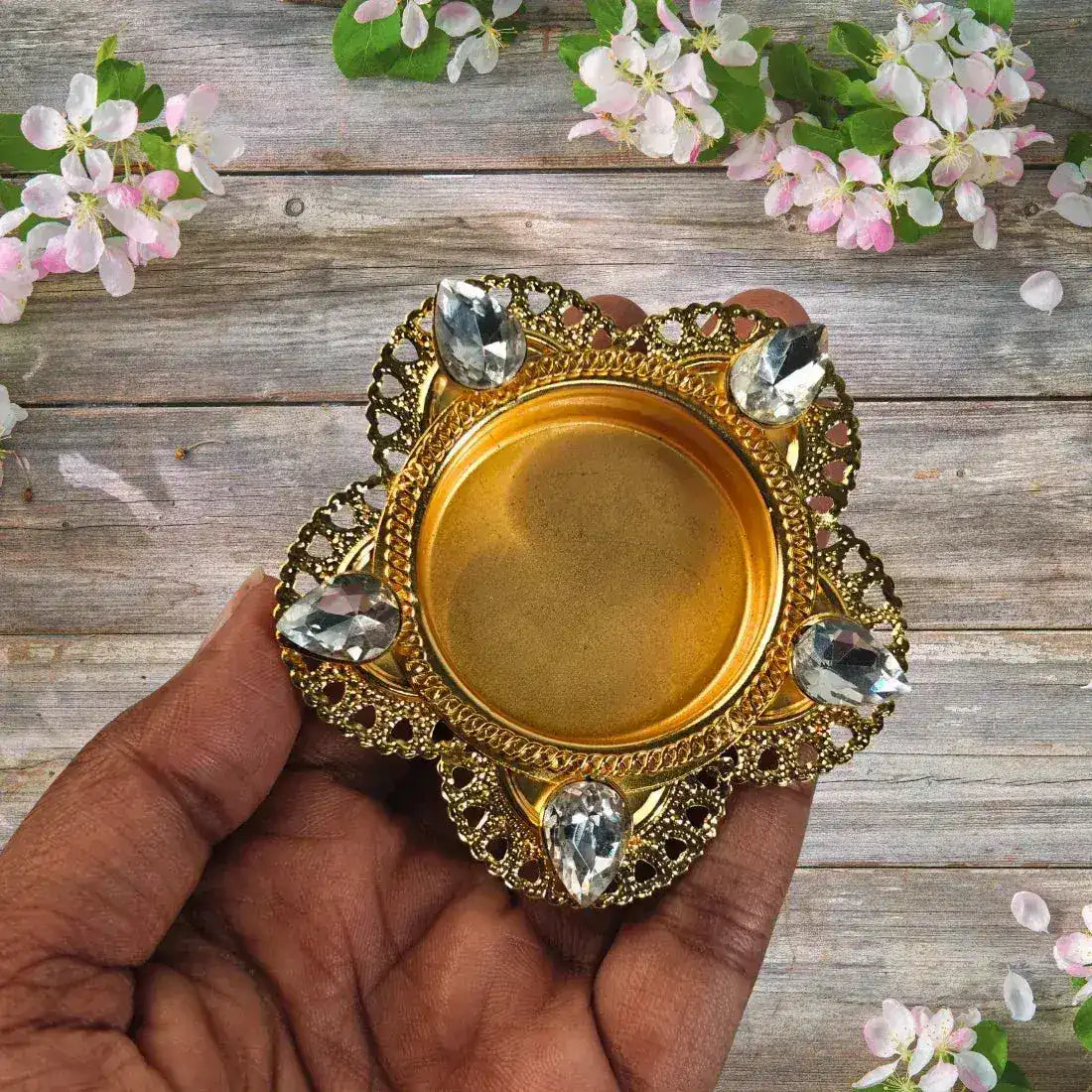 Decorative gold dish held by a hand with flowers in the background
