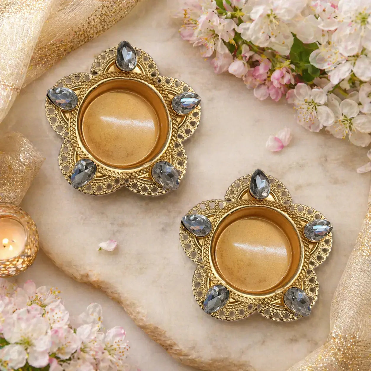 Decorative gold candle holders with gemstones on a marble surface with flowers and candles.