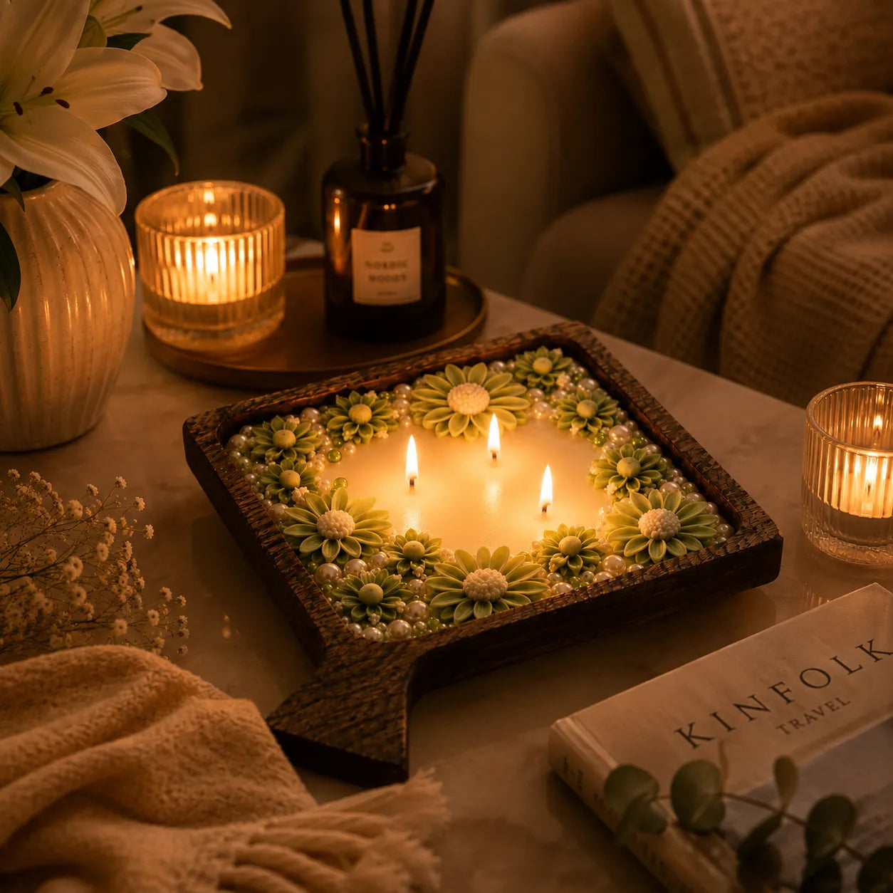 Decorative candle with floral design on a table with candles and a book in the background