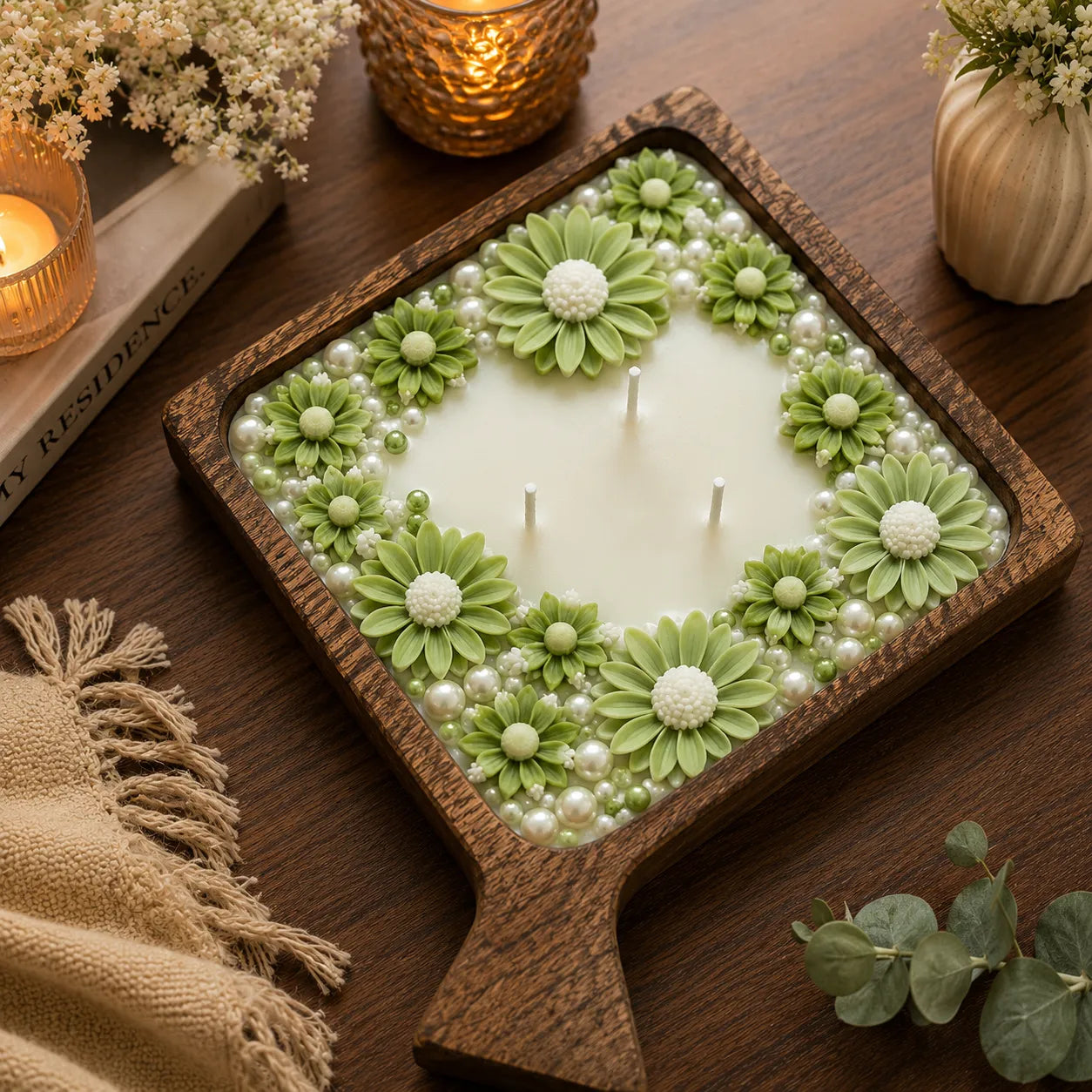 Decorative candle with green floral designs and pearls on a wooden tray.