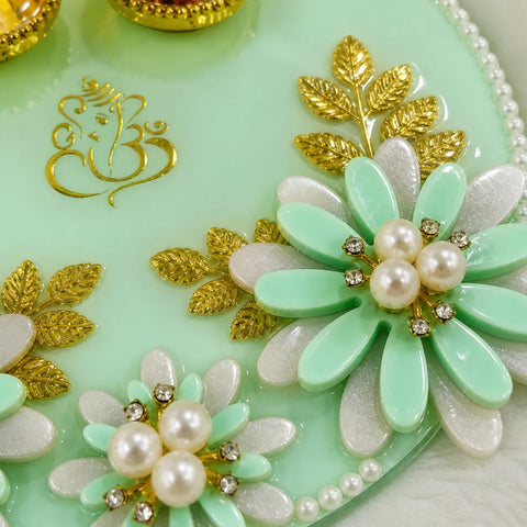 Decorative item with green flowers, gold leaves, and pearls on a light green background