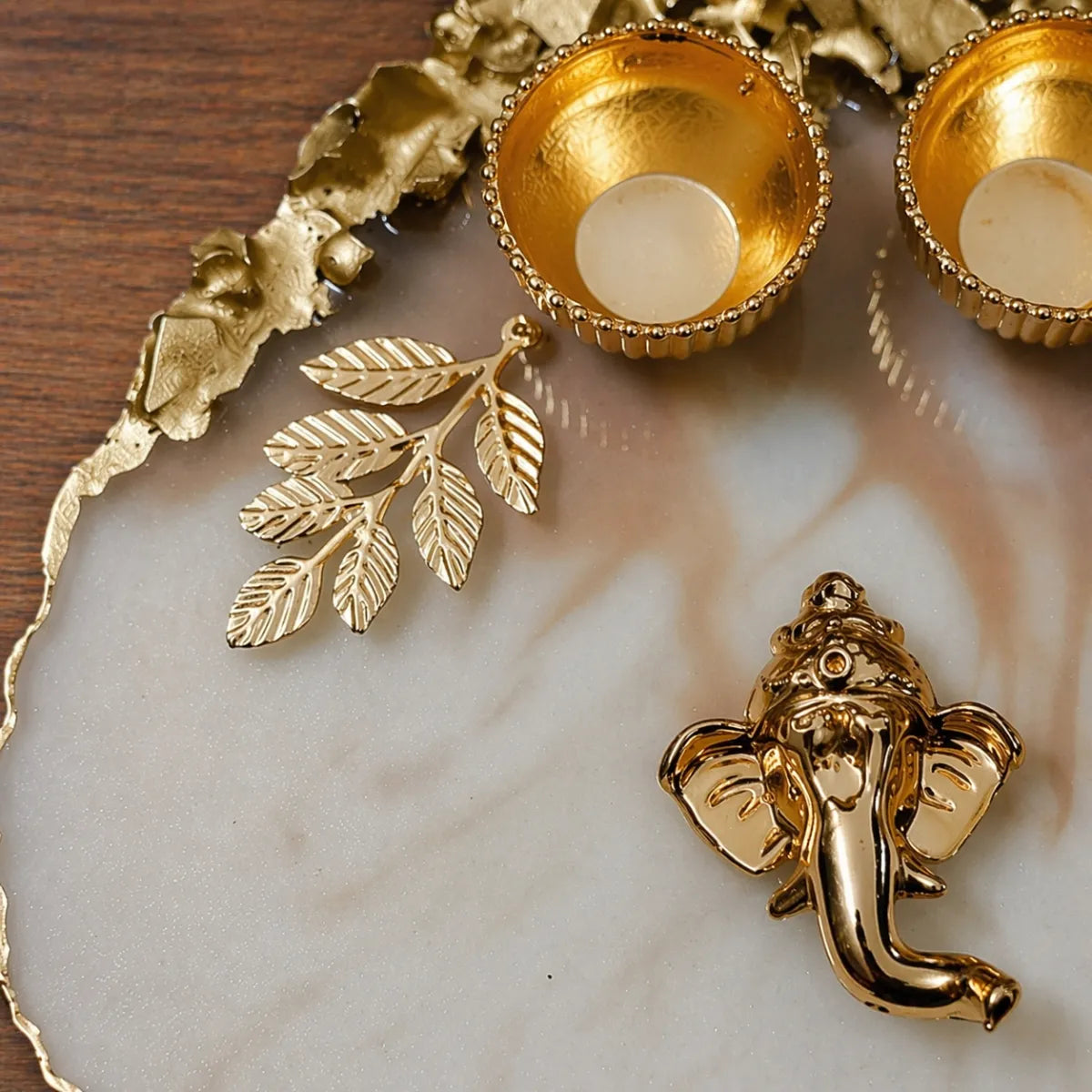 Gold decorative items including leaf earrings and a Ganesha figure on a marble surface.