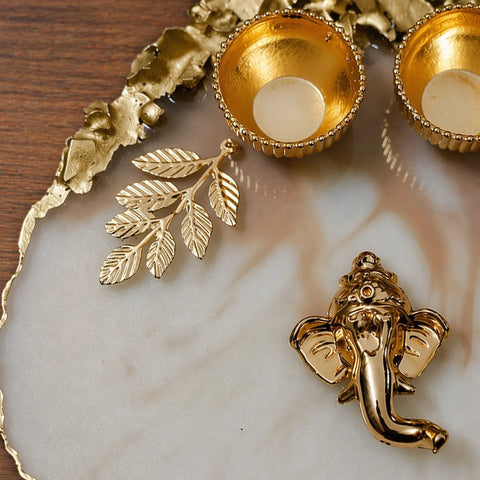 Gold decorative items including leaf earrings and a Ganesha figure on a marble surface.