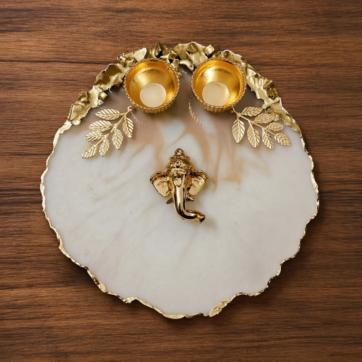 Decorative dish with gold leaf accents, a small statue, and two small bowls on a wooden surface.