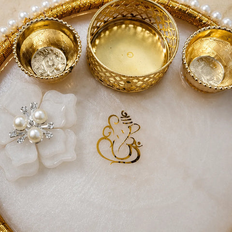 Decorative setting with gold bowls, a brooch, and a Ganesha symbol on a white surface.