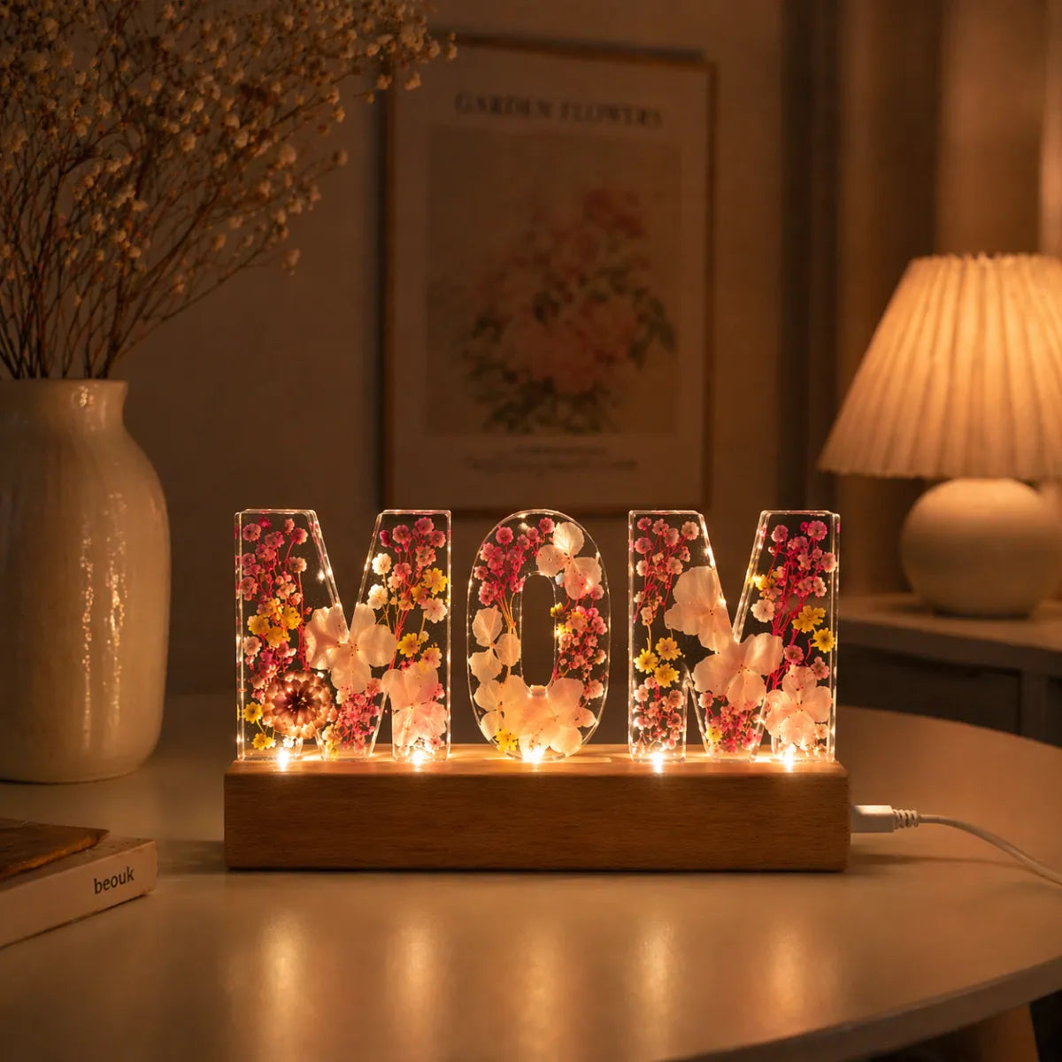 Decorative lamp with 'MOM' letters made of flowers on a table.