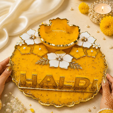 Decorative yellow and white haldi dish with floral designs on a beige background.
