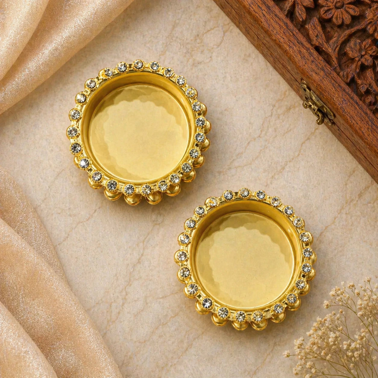 Pair of gold earrings with gemstones on a beige fabric background