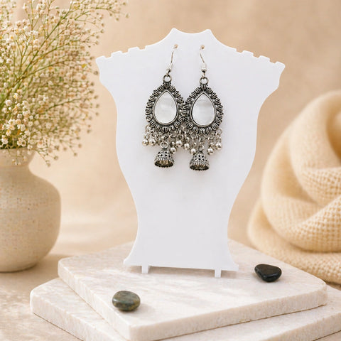 Pair of silver earrings on a white stand with a soft beige background