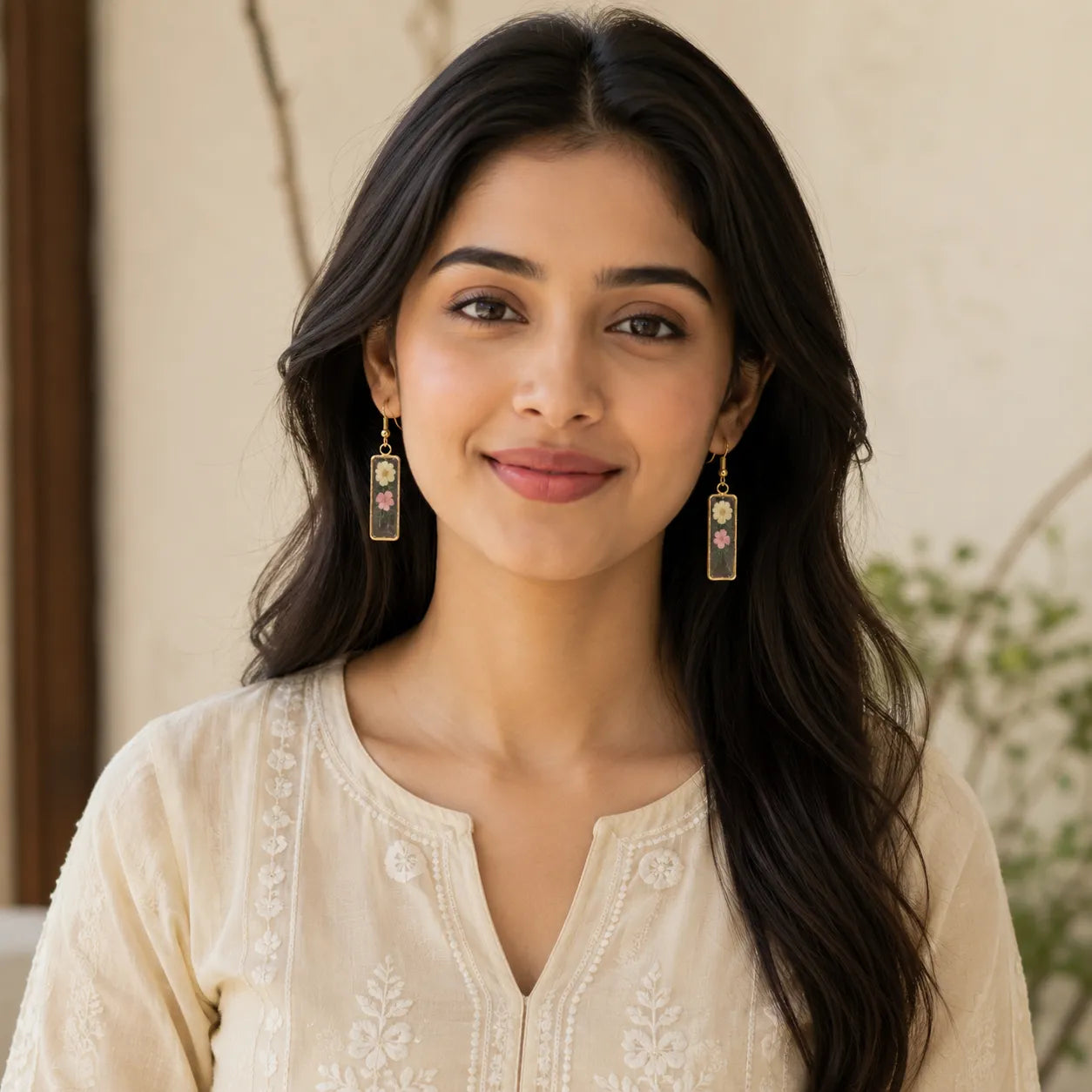 Indian woman wearing floral resin rectangle drop earrings with white and pink dried flowers and elegant gold border design