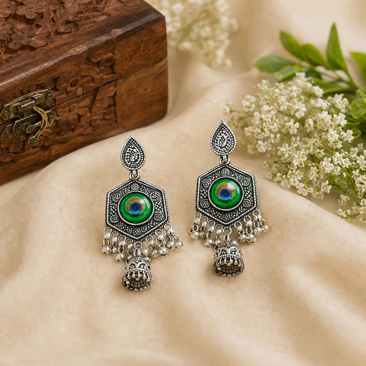 Ornate earrings with green and blue gemstones on a beige fabric background