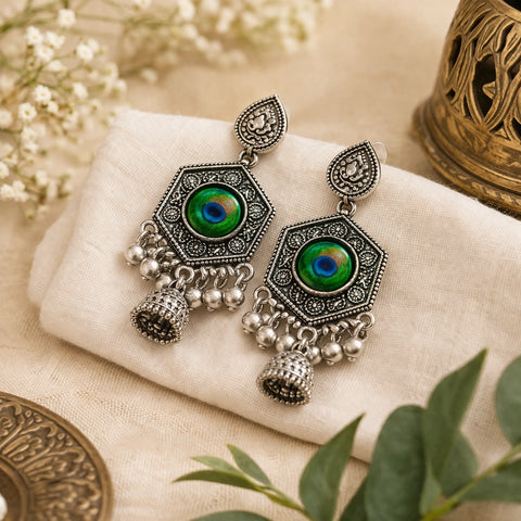 Ornate silver earrings with green gemstones on a beige fabric background