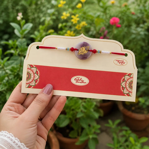 Hand holding a card with a rakhi and decorative elements against a garden background
