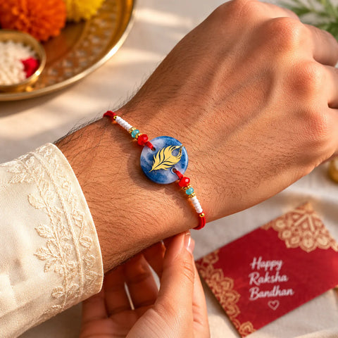 Bracelet with a blue stone and yellow feather design on a wrist, with a 'Happy Raksha Bandhan' card in the background.