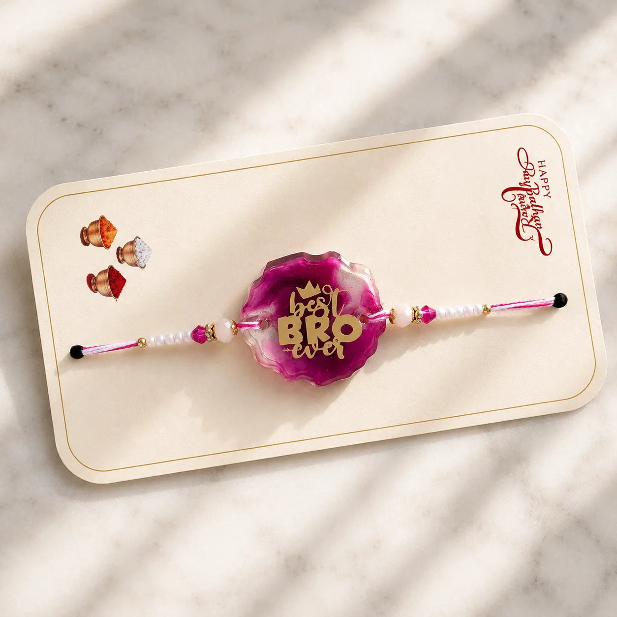 Pink rakhi with 'best bro ever' text on a marble surface