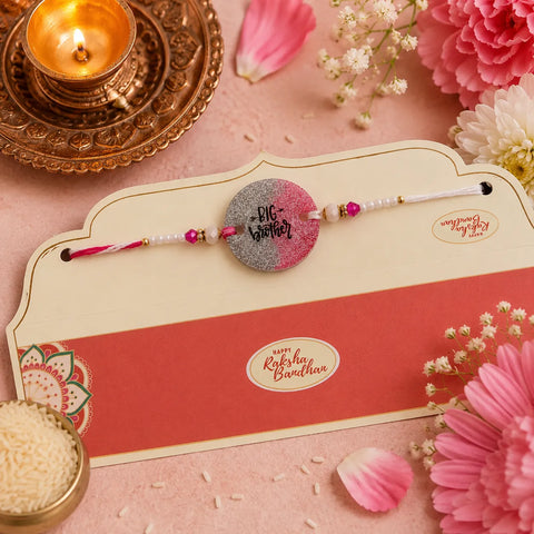 Rakhi with a card on a decorative setting with flowers and a candle.