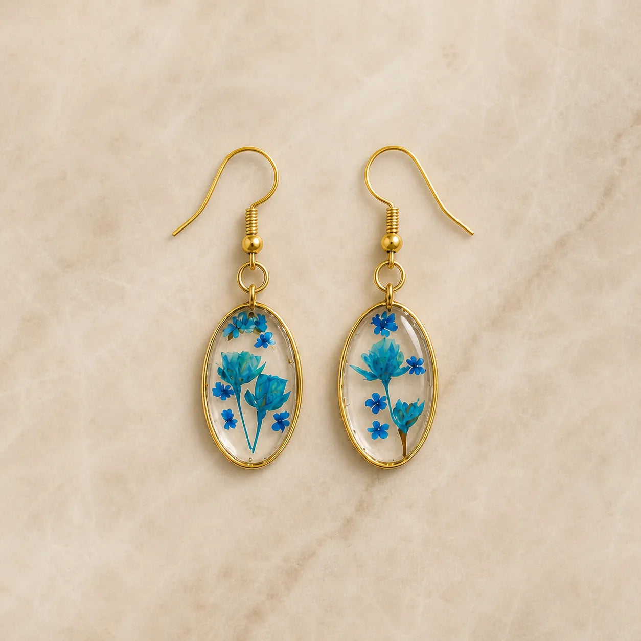 Blue floral resin oval drop earrings with gold frame on beige background, handmade lightweight jewellery for women