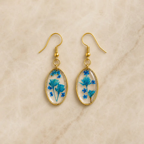 Blue floral resin oval drop earrings with gold frame on beige background, handmade lightweight jewellery for women