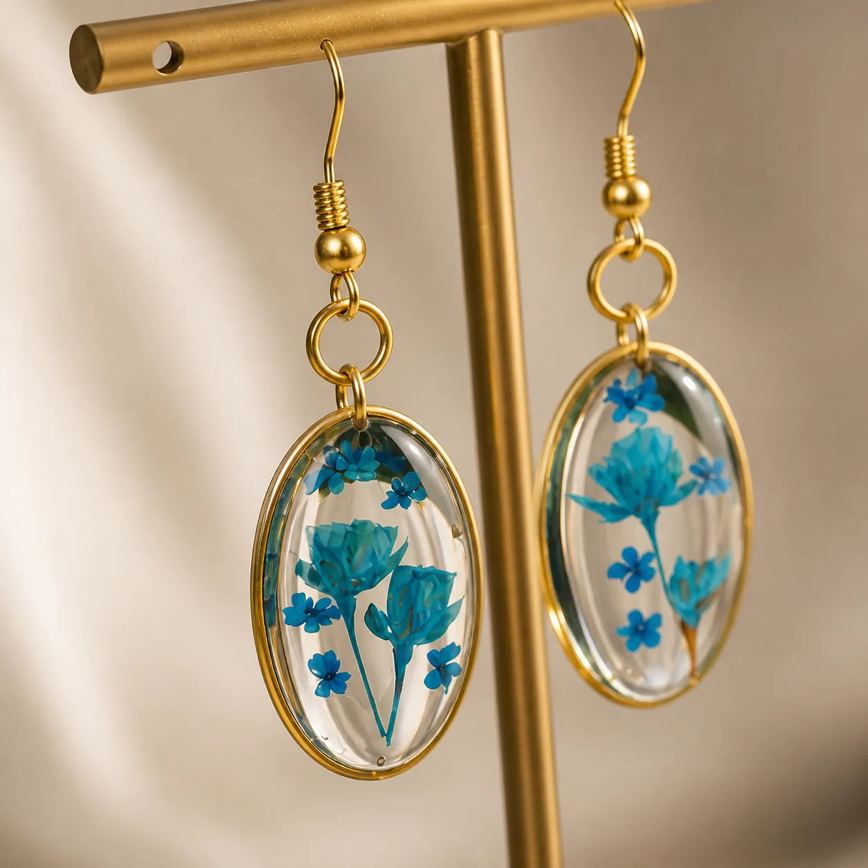 Close-up of blue floral resin oval drop earrings with gold frame, glossy finish handmade jewellery for women