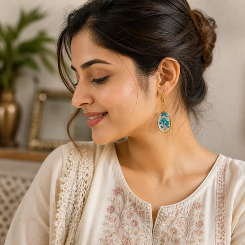 Woman wearing blue floral resin oval drop earrings with gold frame, elegant handmade jewellery lifestyle look