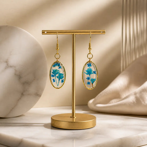 Blue floral resin oval drop earrings displayed on a gold stand with premium beige background, handmade lightweight jewellery for women