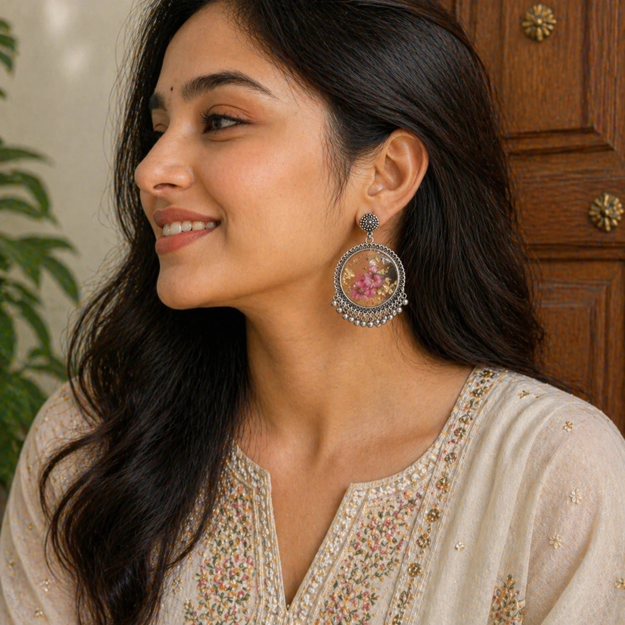 Woman wearing a floral earring with a wooden door and plant in the background