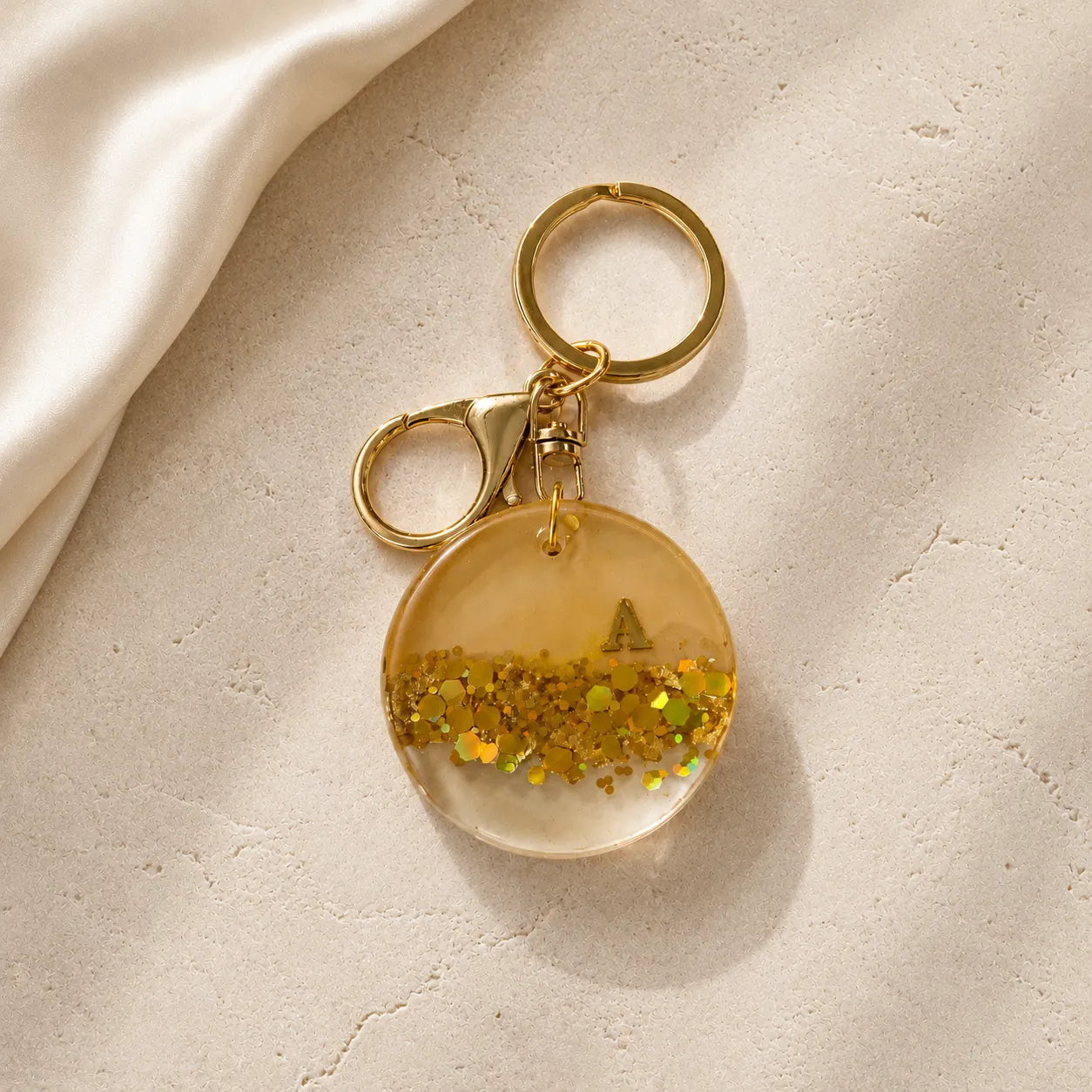 Gold keychain with a clear round pendant and glittery interior on a beige surface