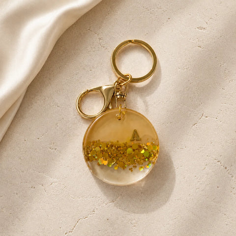 Gold keychain with a clear round pendant and glittery interior on a beige surface
